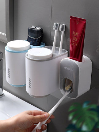 White toothbrush holder with toothbrushes and a tube of toothpaste on a gray wall.